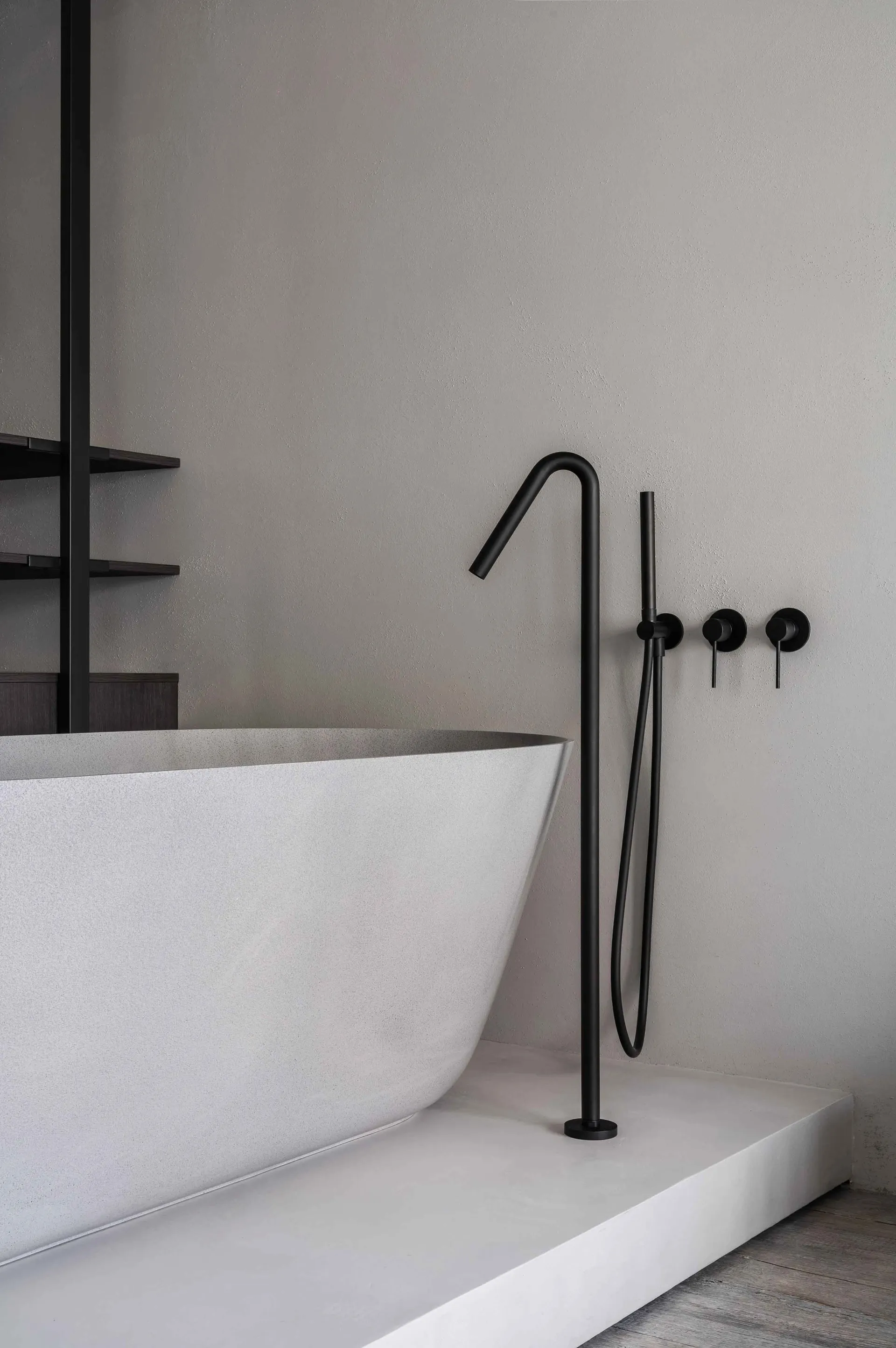 Modern minimalist bathroom featuring a freestanding concrete bathtub with matte black fixtures and a concrete floor.