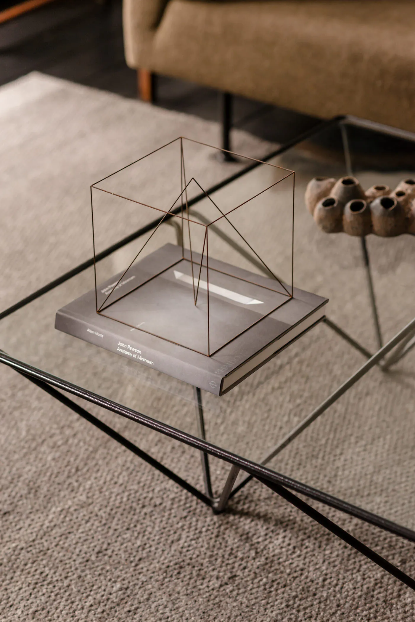 A minimalist metal frame sculpture on top of a book in a living room setting.