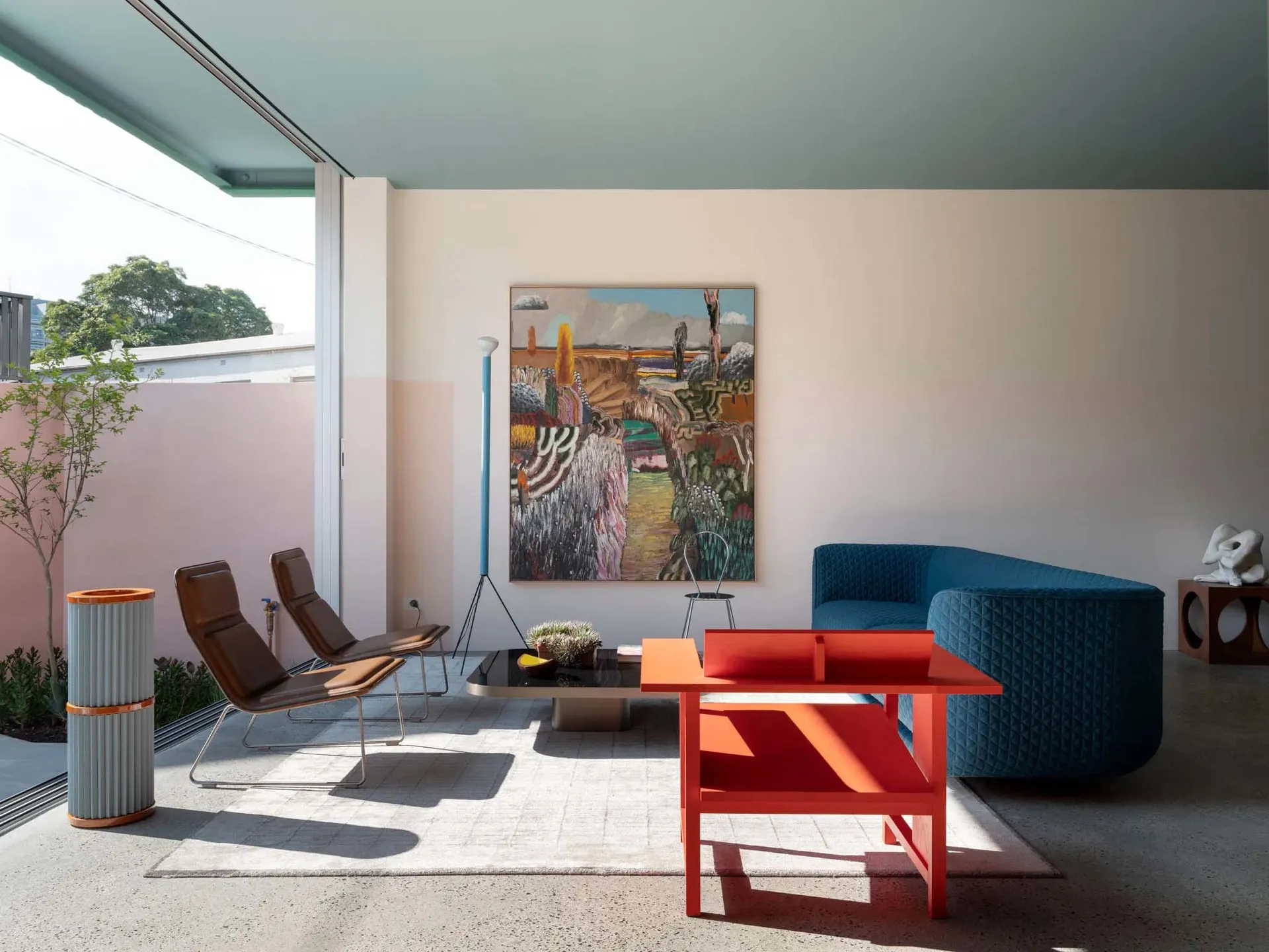 A modern living room featuring metal chairs, a fabric sofa, and wooden coffee table and side tables with plants and artwork.