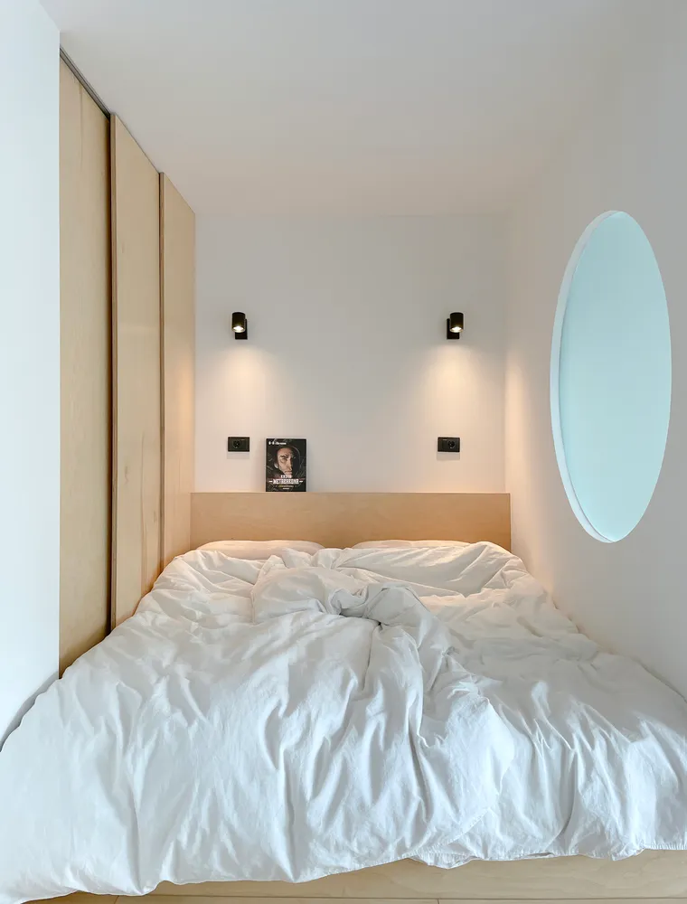 A minimalist bedroom with white walls, a wooden bed frame, and white towels.