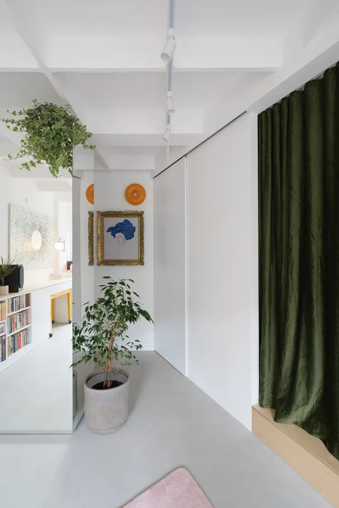 A modern minimalist living space with white concrete walls, a large green curtain, and a potted plant.