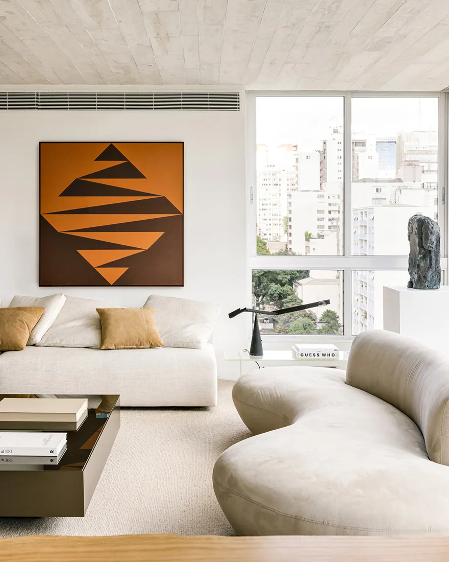 Modern, minimalist living room featuring a white fabric sofa, abstract art, and a view of the city through large windows.