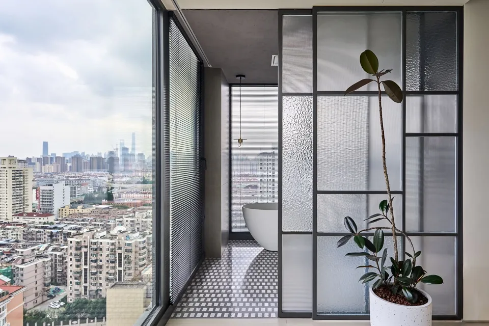 Modern minimalist bathroom featuring glass walls, concrete tiles, and a white bathtub.