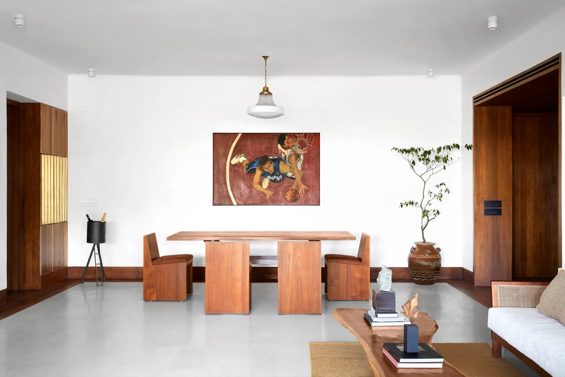 A minimalist living room with wooden furniture and a concrete floor, featuring a basketball painting on the wall.
