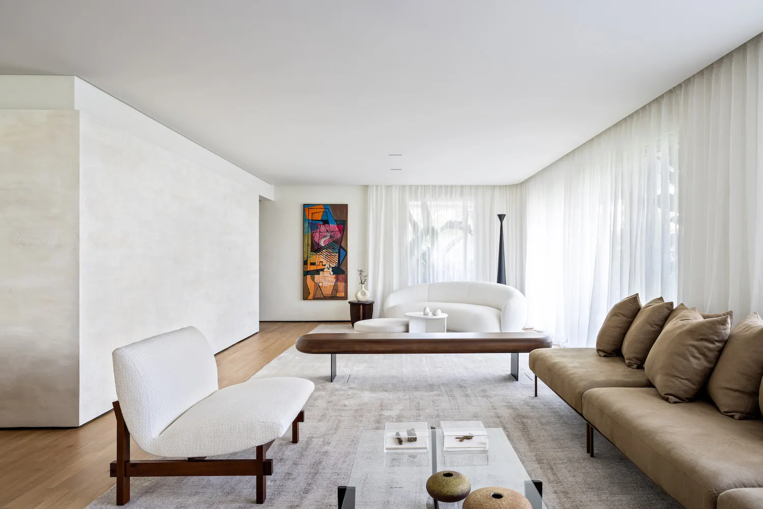 A modern minimalist living room with a glass coffee table and sleek furniture, featuring light-colored walls and a white rug.