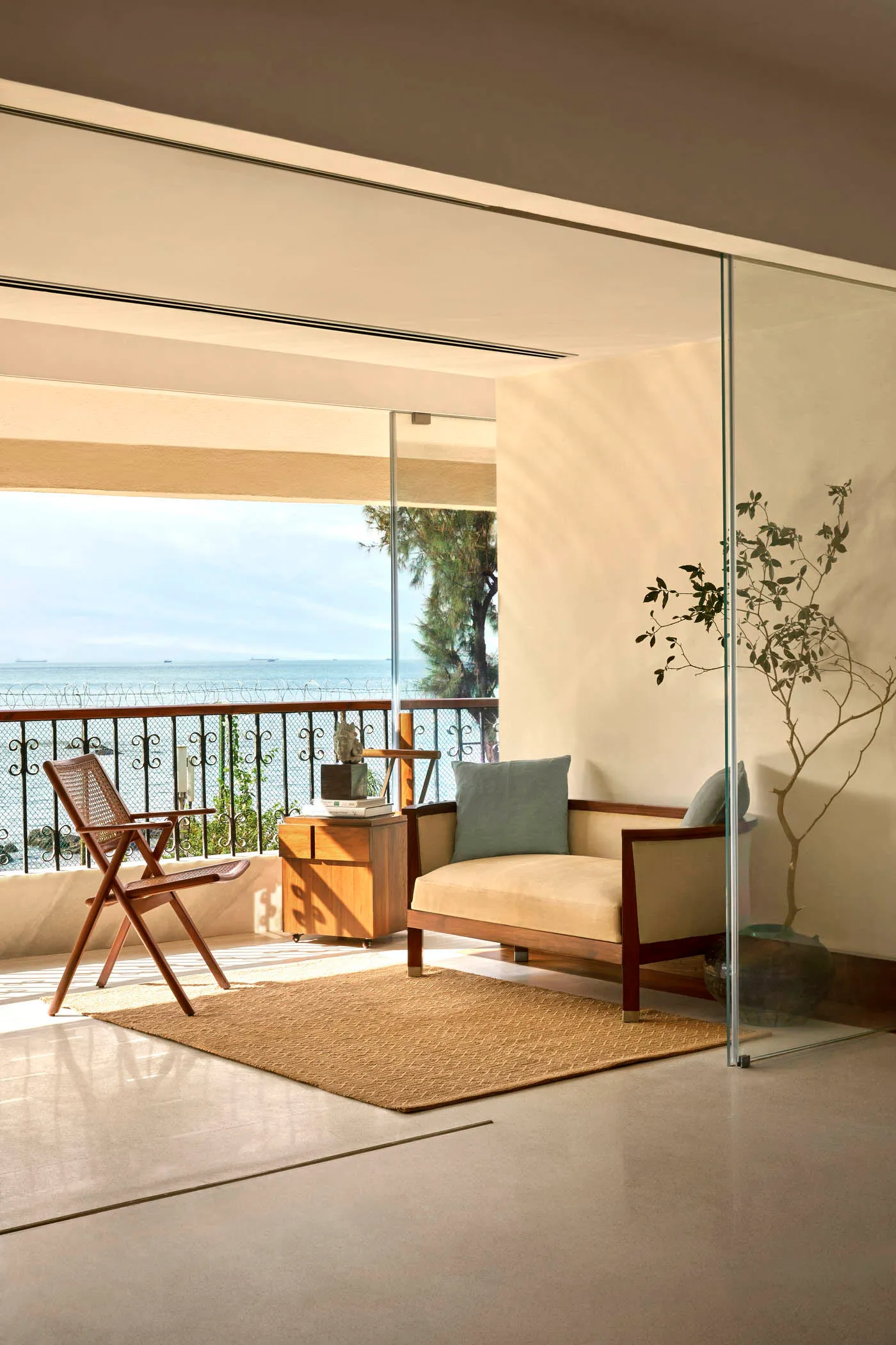 A minimalist living room featuring natural wood furniture, a glass partition, and a view of the ocean.