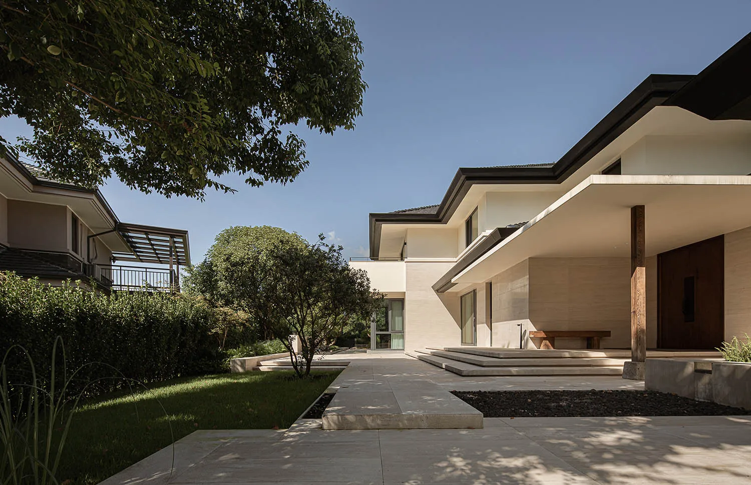 A modern residential architecture featuring minimalist design, glass walls, and a lush green lawn.