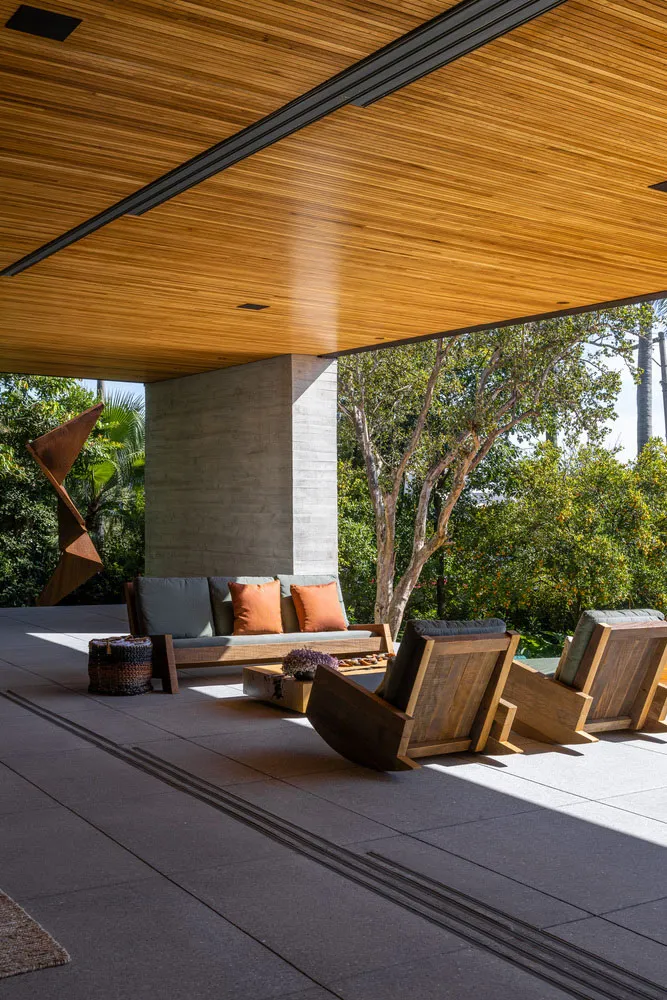 A modern minimalist outdoor lounge area featuring wooden furniture and a concrete pillar.