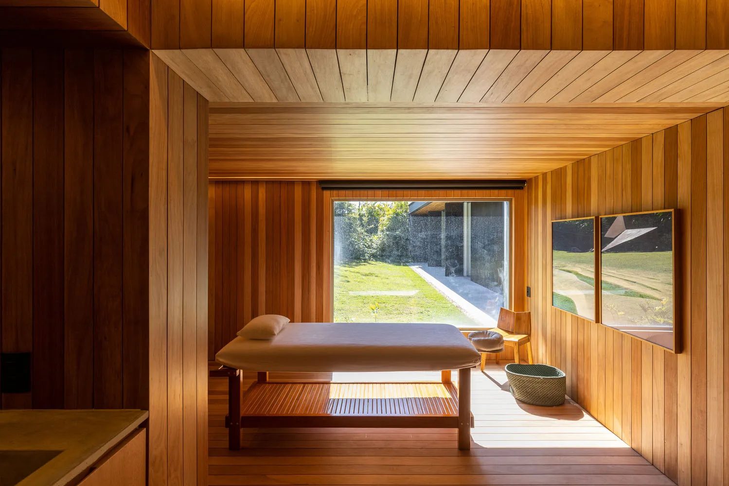 A modern spa room featuring a wooden treatment bed and natural light from a large window.
