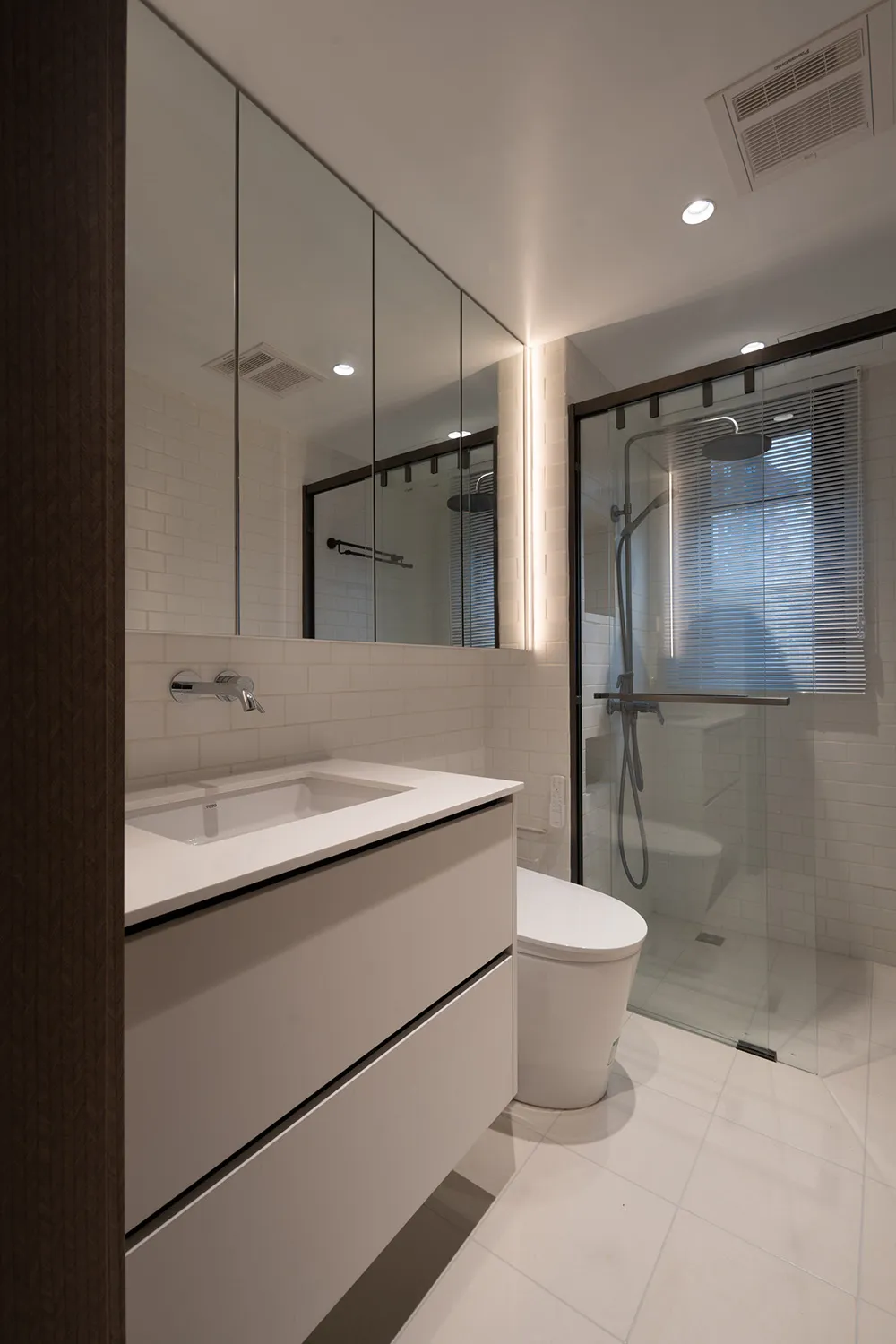 A modern bathroom with white tiles and white fixtures, featuring a white porcelain toilet, a white ceramic sink, white porcel