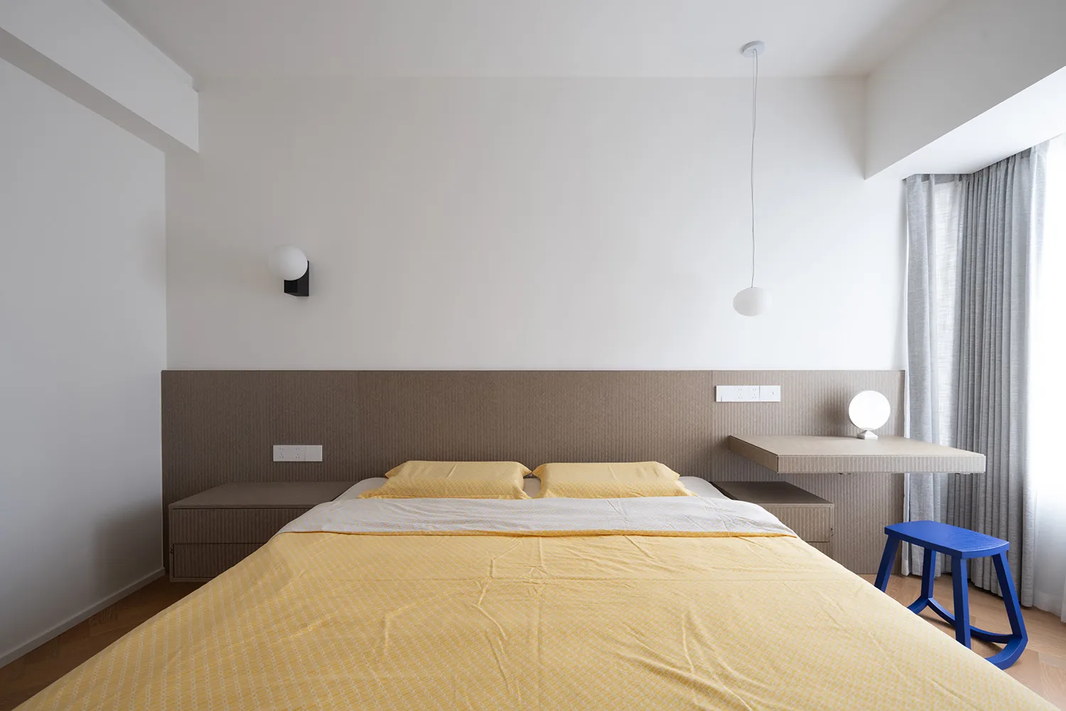 A modern bedroom interior with a yellow bedspread and a textured fabric headboard.