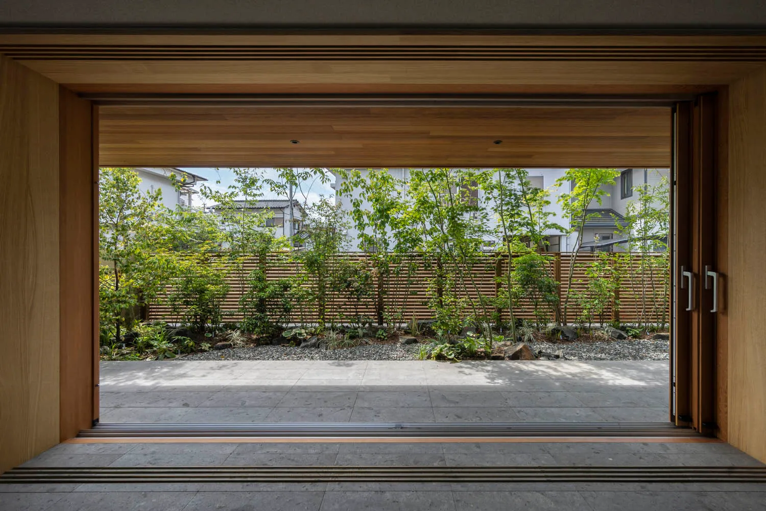 A modern garden with hardwood flooring and plants, viewed from a wooden doorway.
