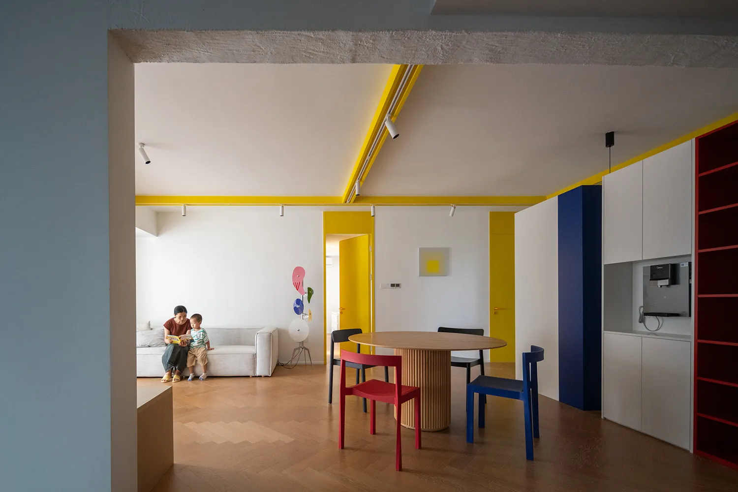 A modern residential space featuring wood furniture and yellow accents, with a sofa and child sitting together on a couch, a