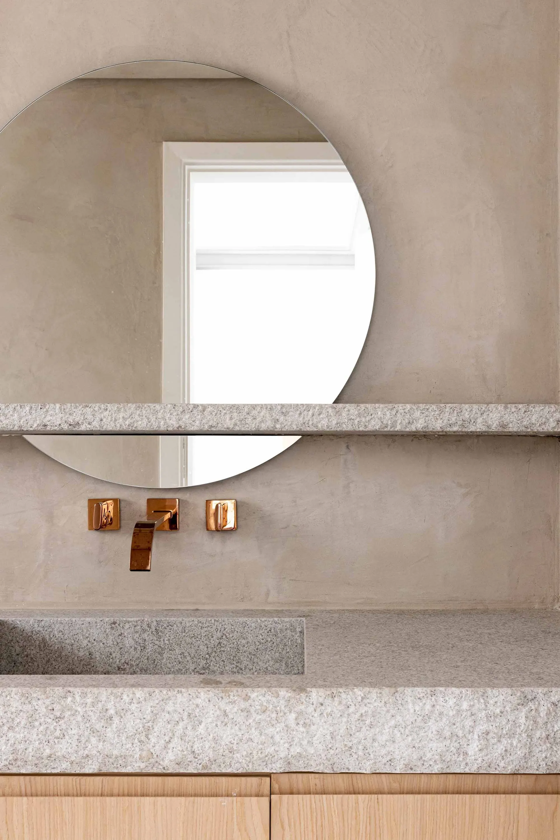 Modern minimalist bathroom featuring a concrete countertop and sink with a round mirror and brass fixtures.