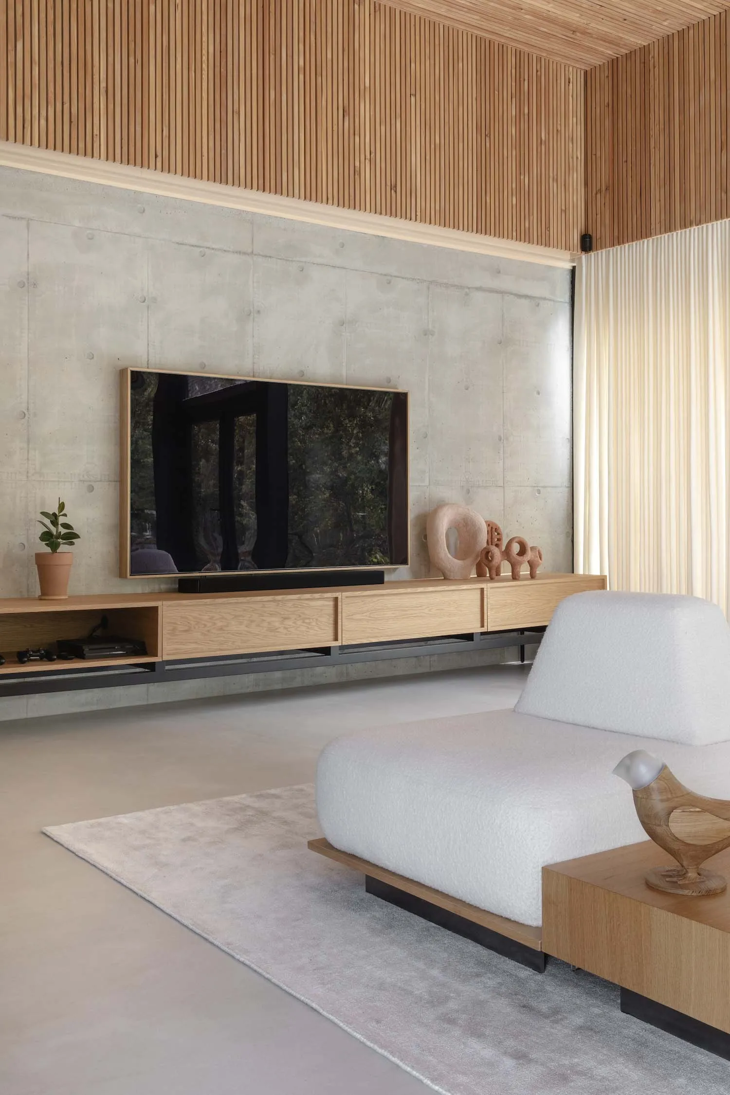 A modern, minimalist living room with concrete walls and a wooden TV stand and furniture.