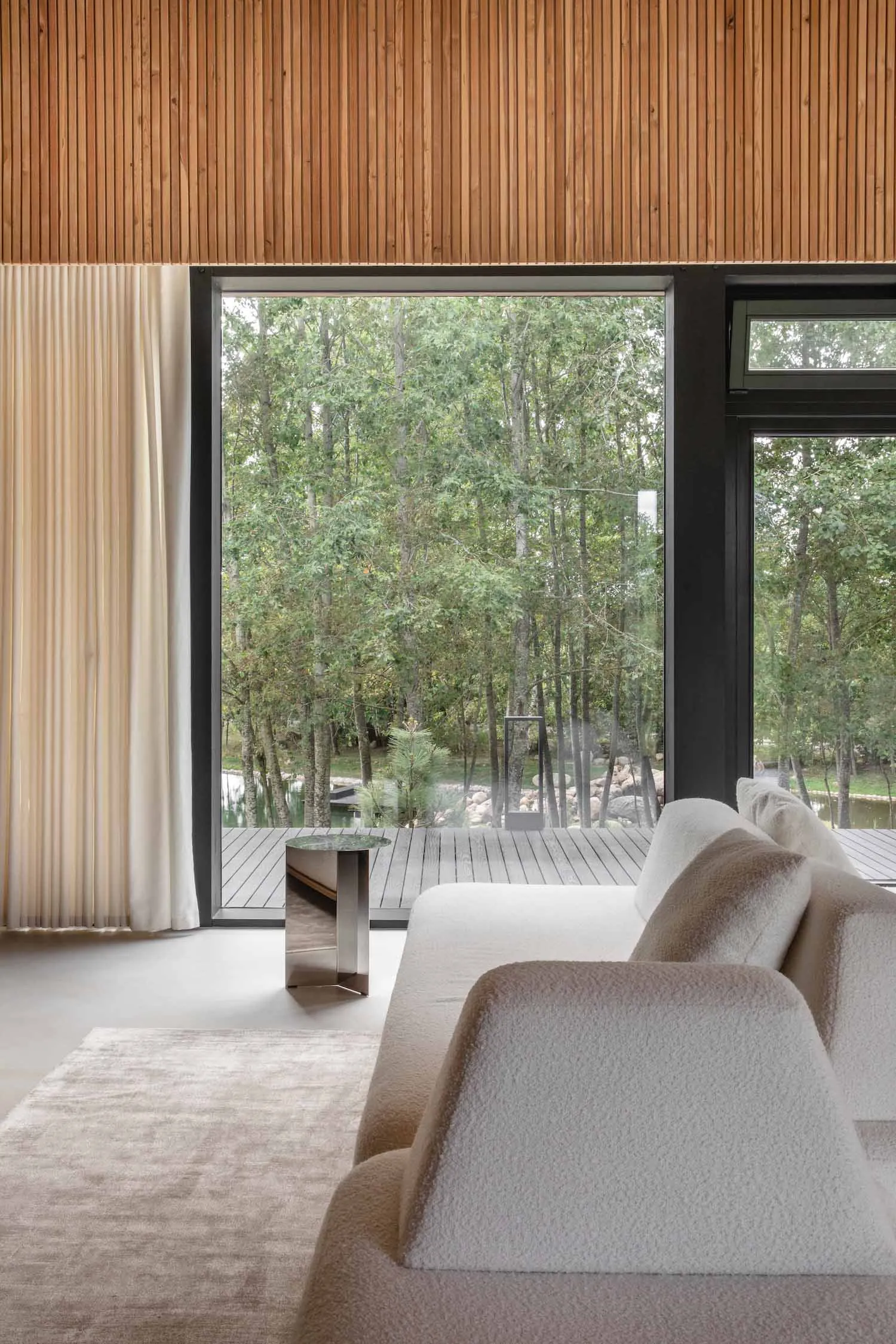 Modern living room with wooden walls and a view of the forest through large windows.