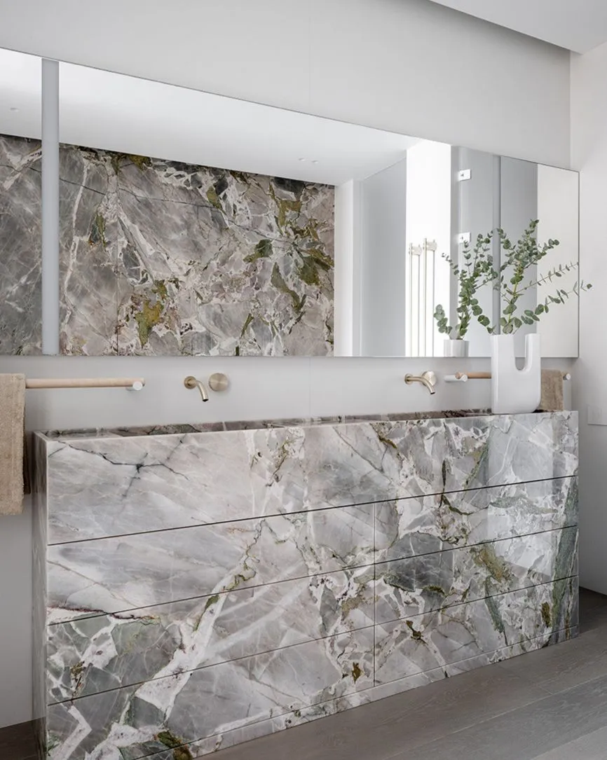 A minimalist bathroom featuring marble walls and countertops with natural light.