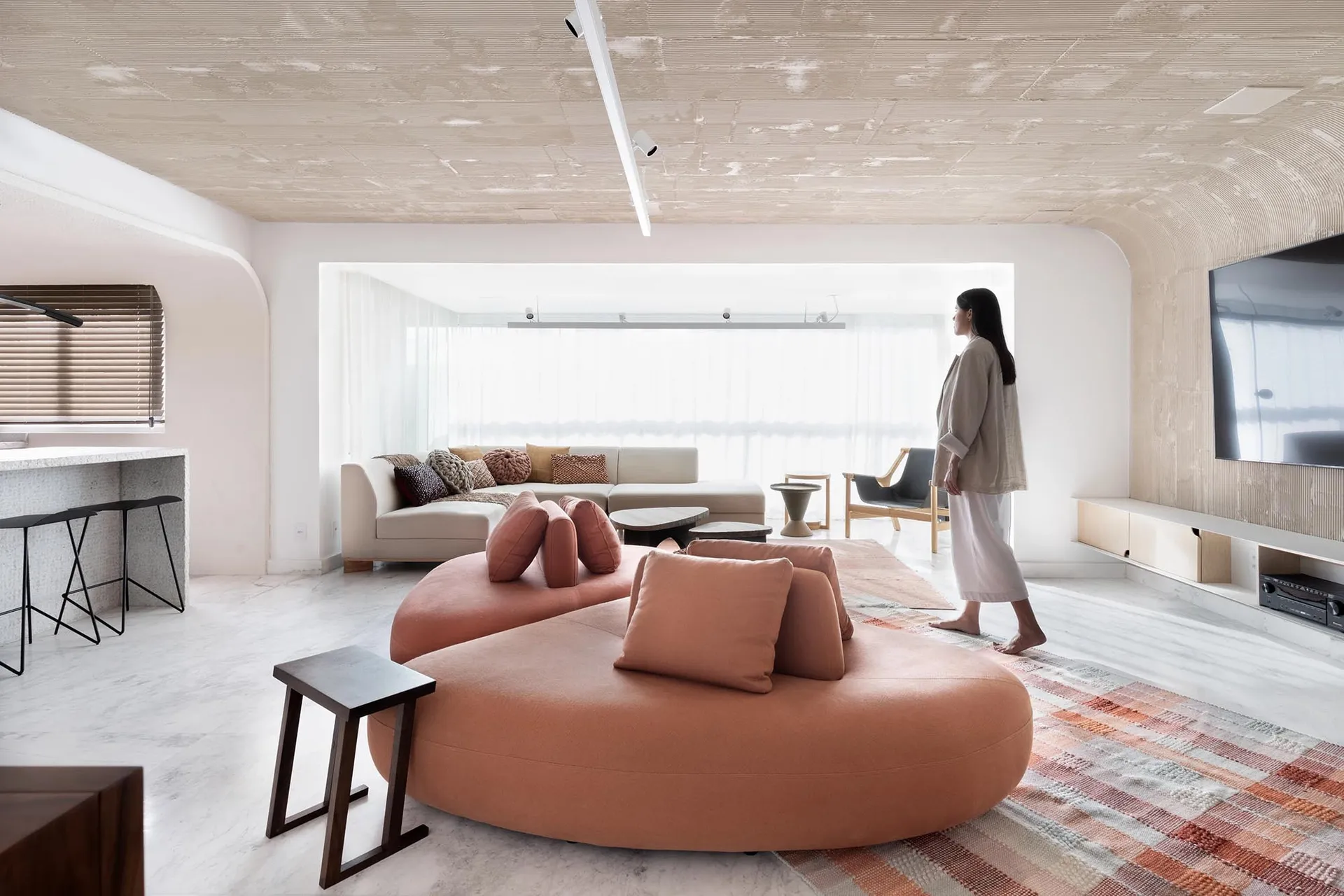A modern living room with a large circular sofa upholstered in fabric, accompanied by a coffee table and side tables. The roo