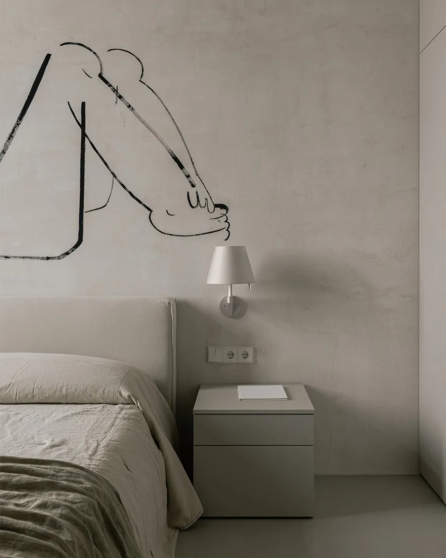 A minimalist bedroom featuring a bed with light-colored bedding, a concrete headboard, and a bedside table with a lamp.