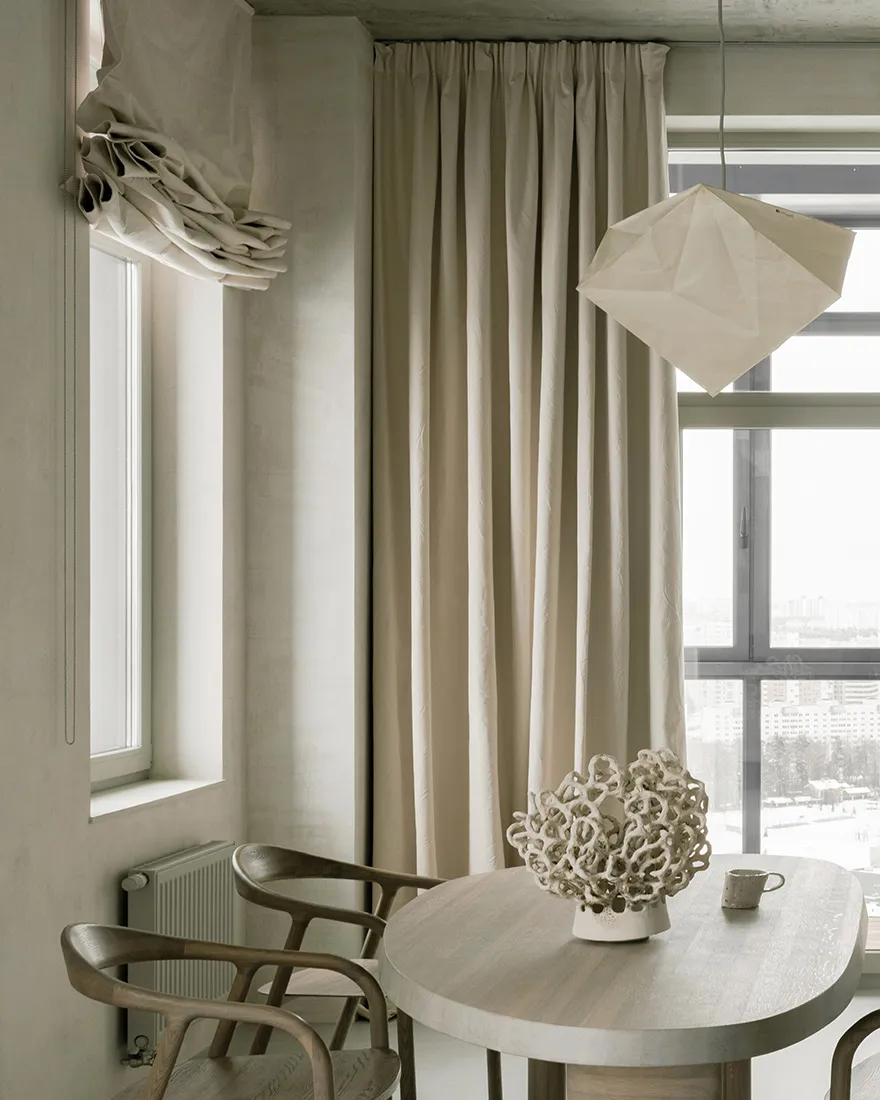 A minimalist dining room with a round wooden table, a concrete floor, and paper lampshade.