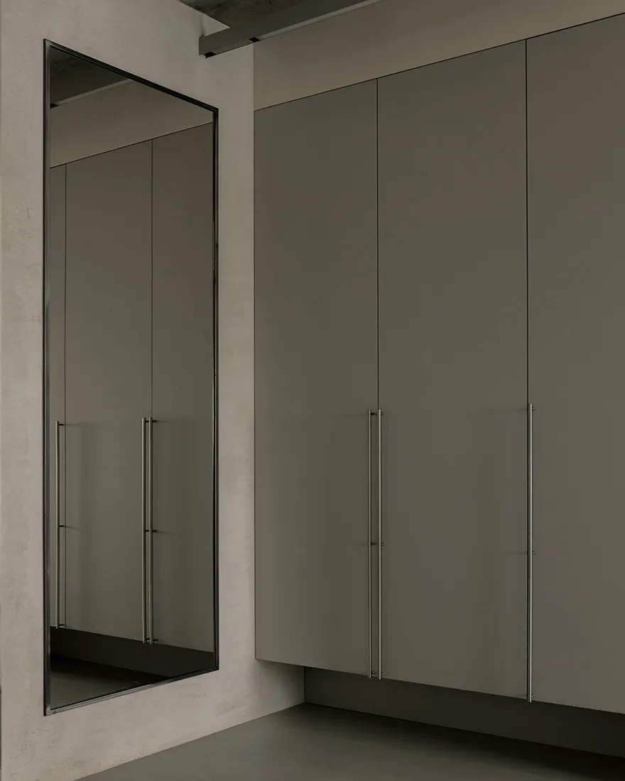 A minimalist interior design featuring a concrete wall and floor, with a large mirror and a cabinet.