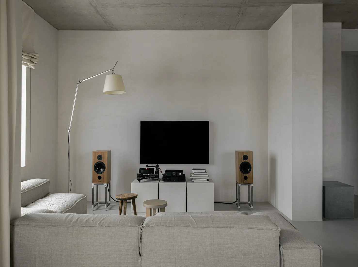 A minimalist living room with concrete walls, a large sofa, and floor-to-ceiling windows.