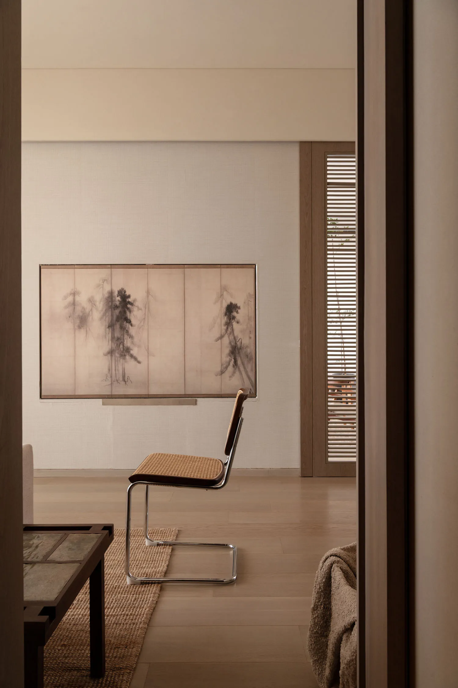 A modern living room featuring a wooden dining table with chairs, a bonsai tree, and sheer curtains allowing natural light to
