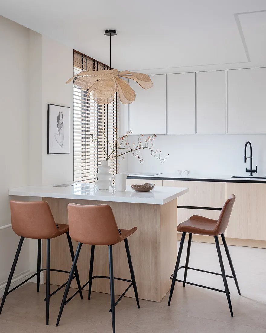 A modern minimalist kitchen with wooden finishes, a hanging woven ceiling lamp, and brown leather bar stools.