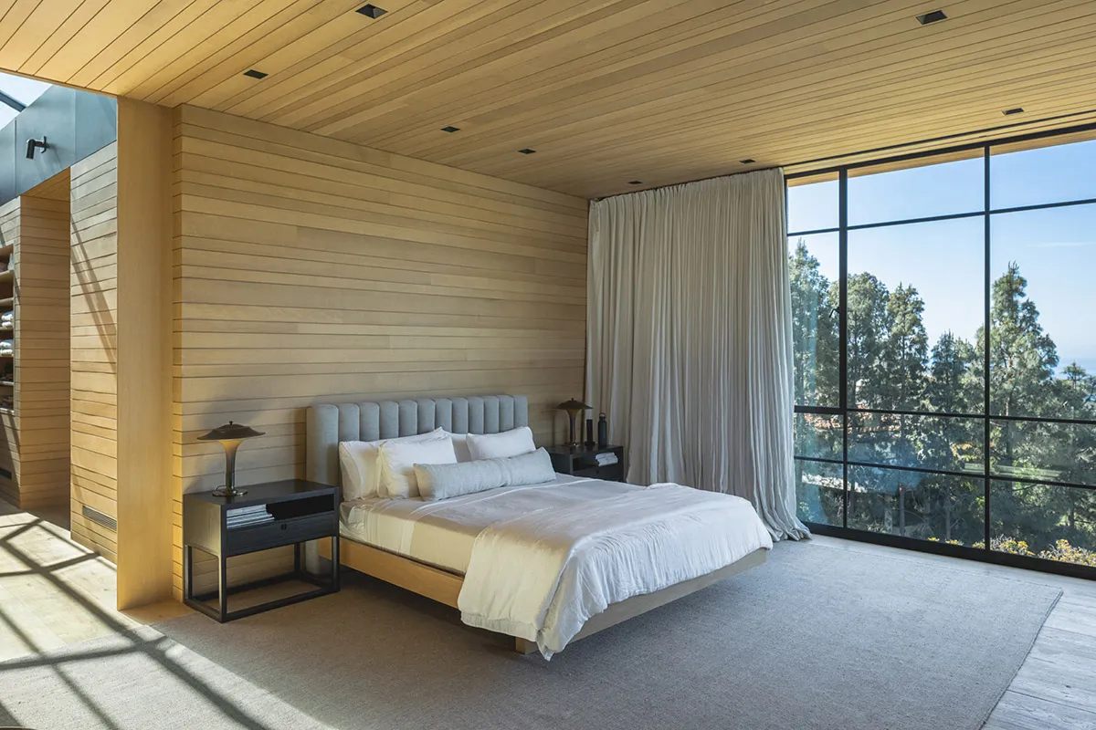 Modern bedroom featuring a minimalist design with wooden walls and a large window showcasing a scenic view.