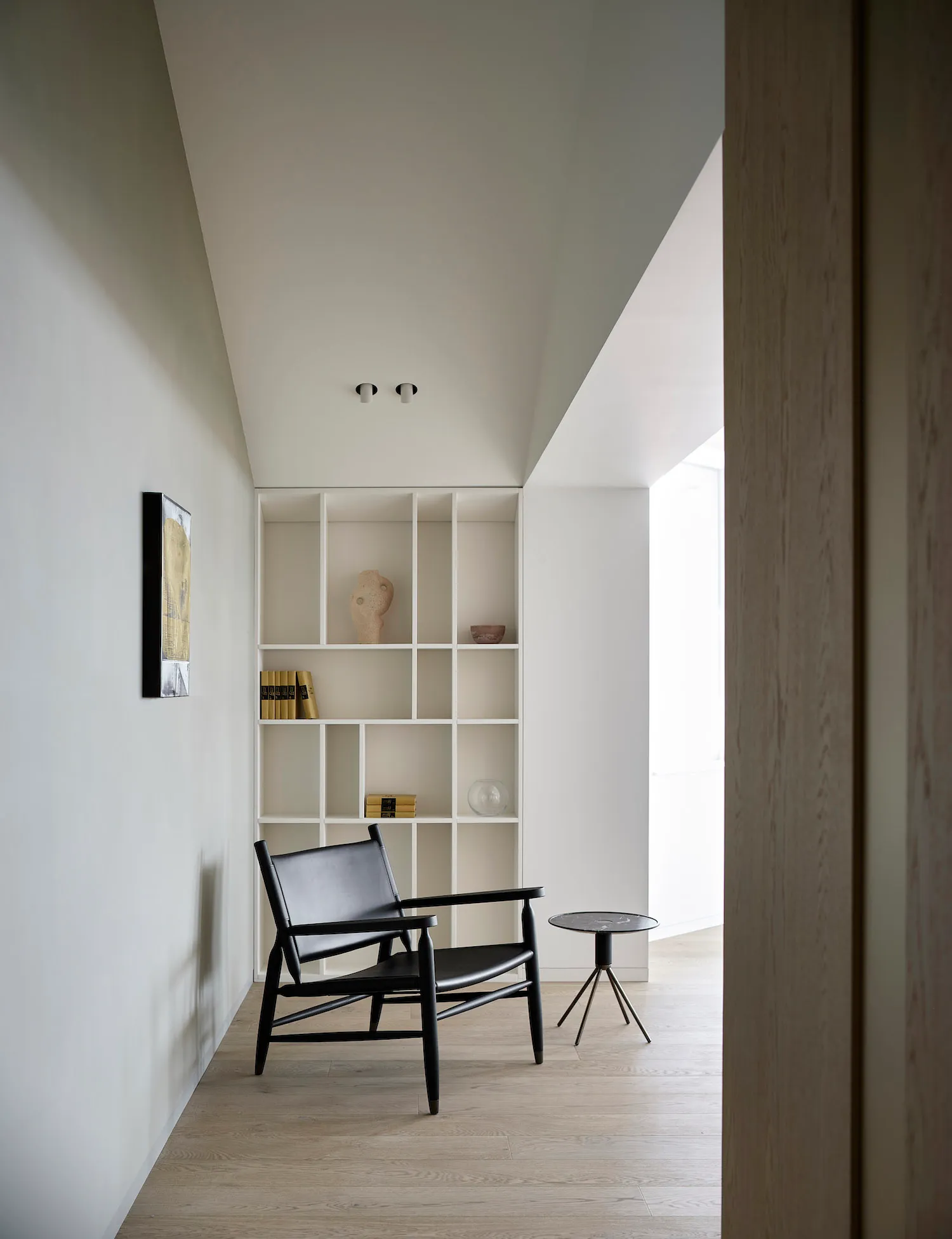 Modern minimalist home entry with a black armchair, white shelving unit, and wooden floor.