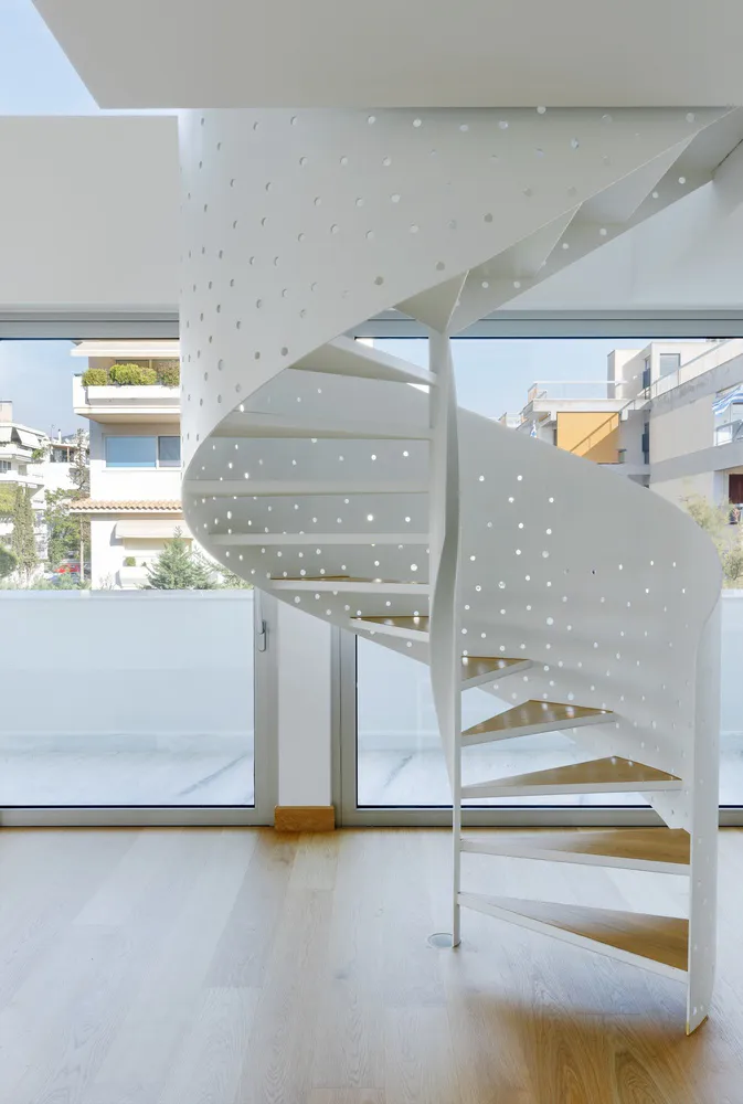A modern metal staircase with perforated railings and wooden steps, set against a bright, airy background.