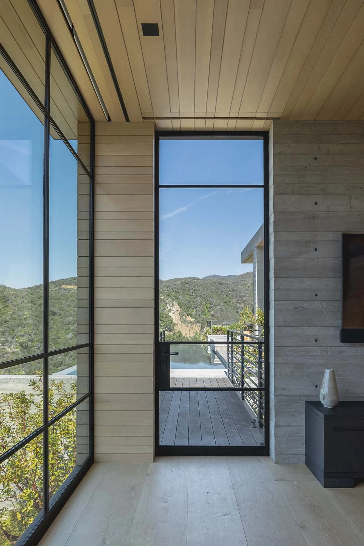A modern interior with a wooden wall and large glass door leading to a wooden deck overlooking a scenic landscape.