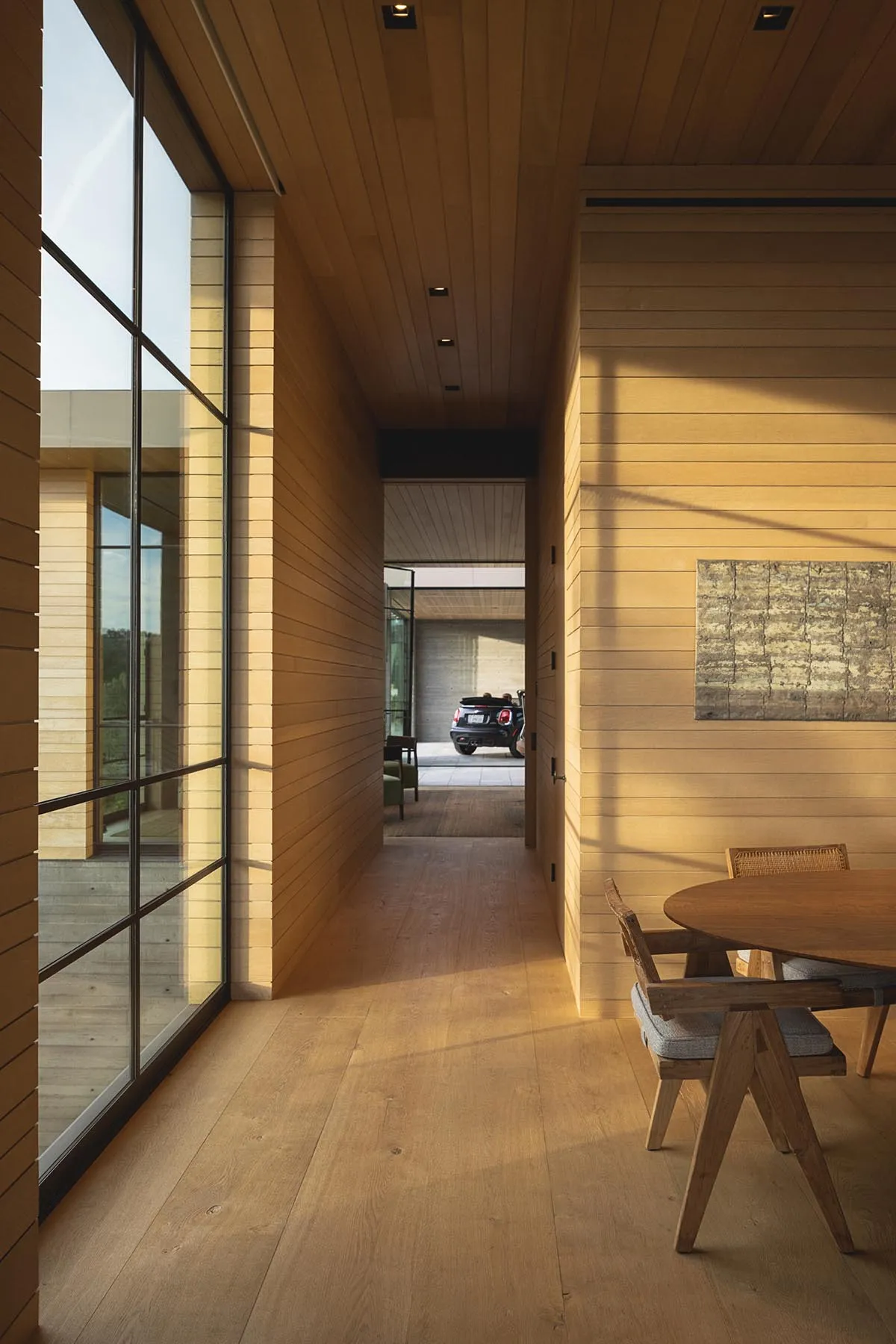 Modern minimalist dining room featuring wooden paneling and large glass windows.