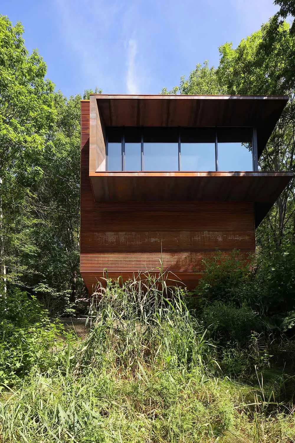 Modern residential house with steel exterior and large windows in a forest setting.