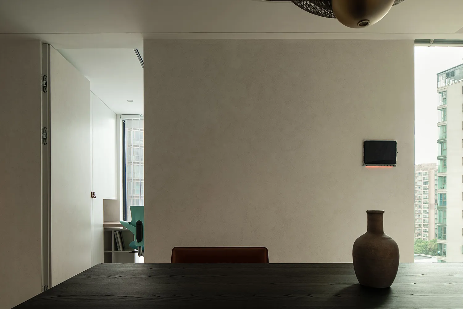 Minimalist dining room featuring dark wood table and modern chair against a plain wall and large window.