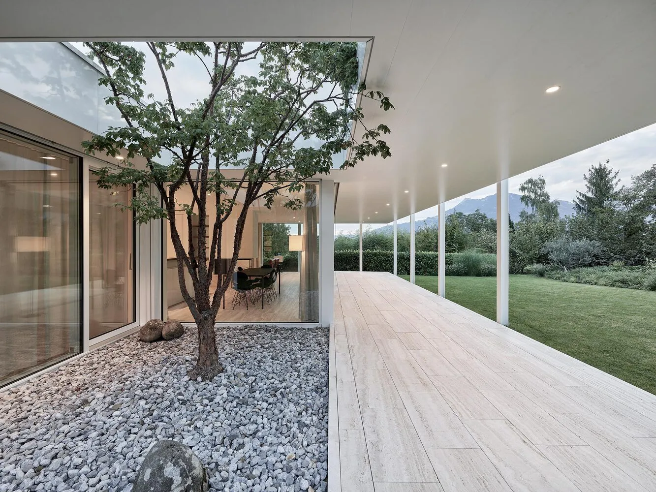A modern residential building featuring a glass exterior with a tree in the center courtyard.