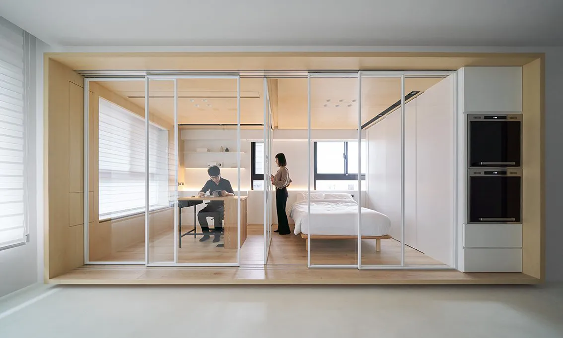 A minimalist bedroom with wood finishes and metal accents, featuring a white bed and a person standing near a window.