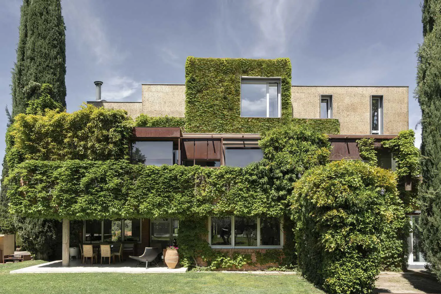 A modern residential exterior covered in climbing plants.