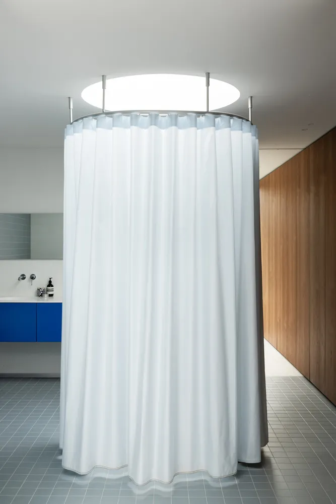A minimalist bathroom featuring a white fabric shower curtain with a circular light fixture above it.