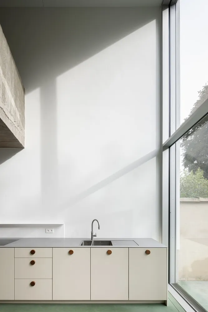 Modern kitchen featuring minimalist design with concrete walls and white cabinetry.