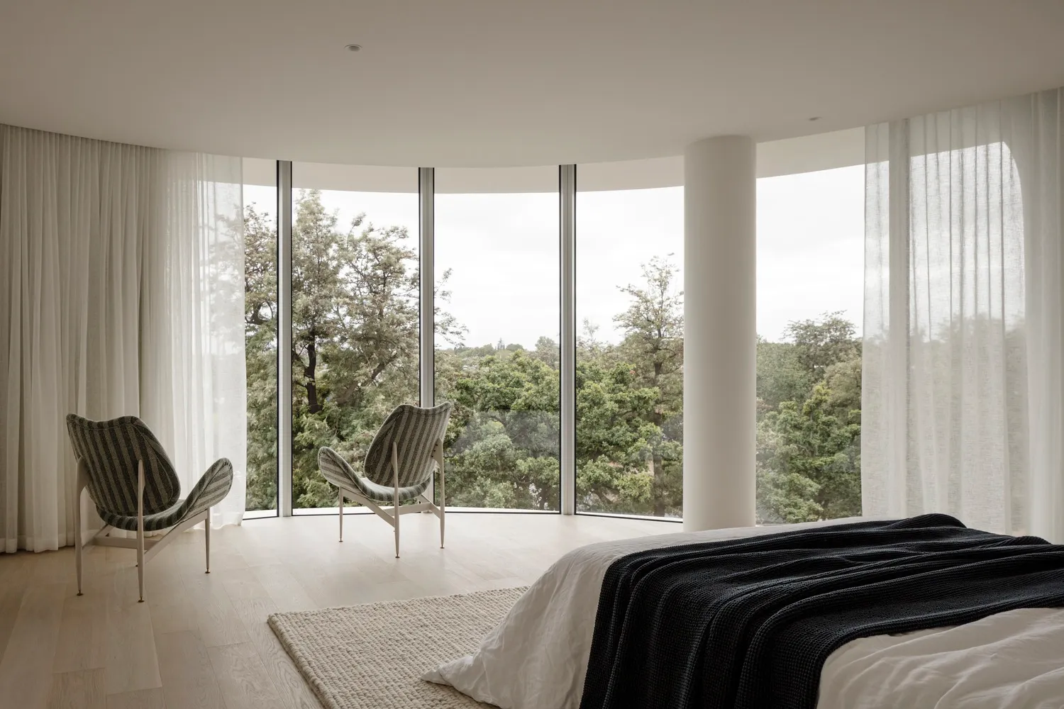 Modern bedroom featuring a glass-enclosed floor-to-ceiling window, wooden flooring, and fabric furniture.