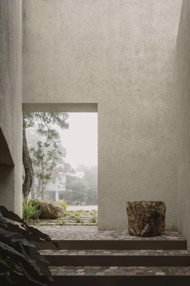 Modern exterior view of a building with a textured concrete wall and a pathway leading to a garden.