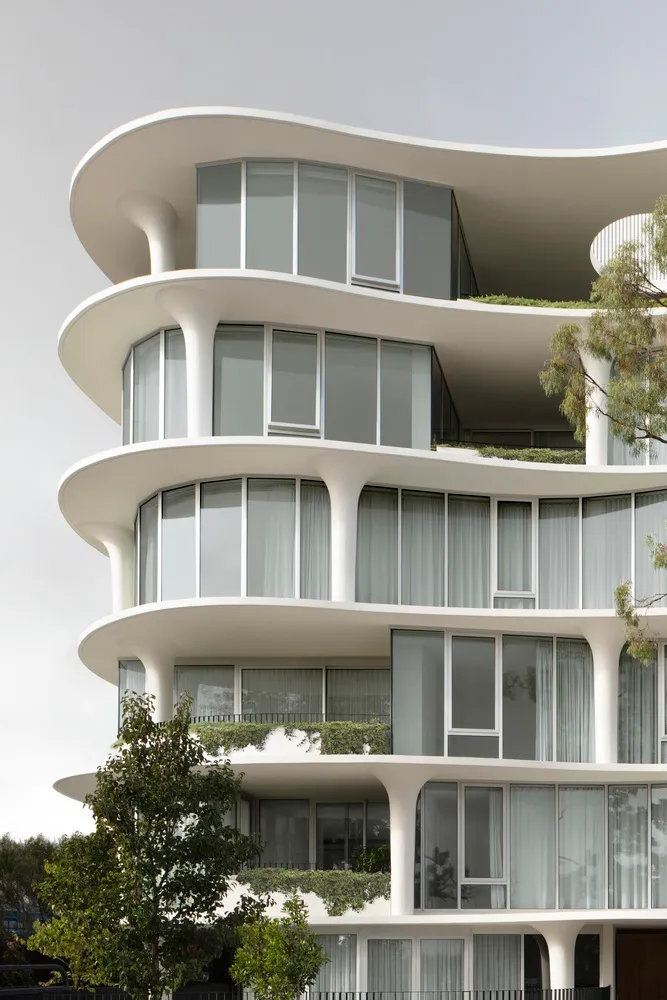 Modern apartment building with glass balconies and white columns against a cloudy sky.