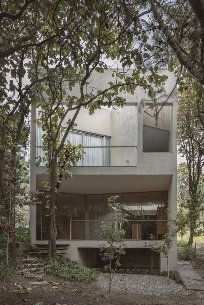 A modern, minimalist residence with a concrete exterior surrounded by lush greenery.