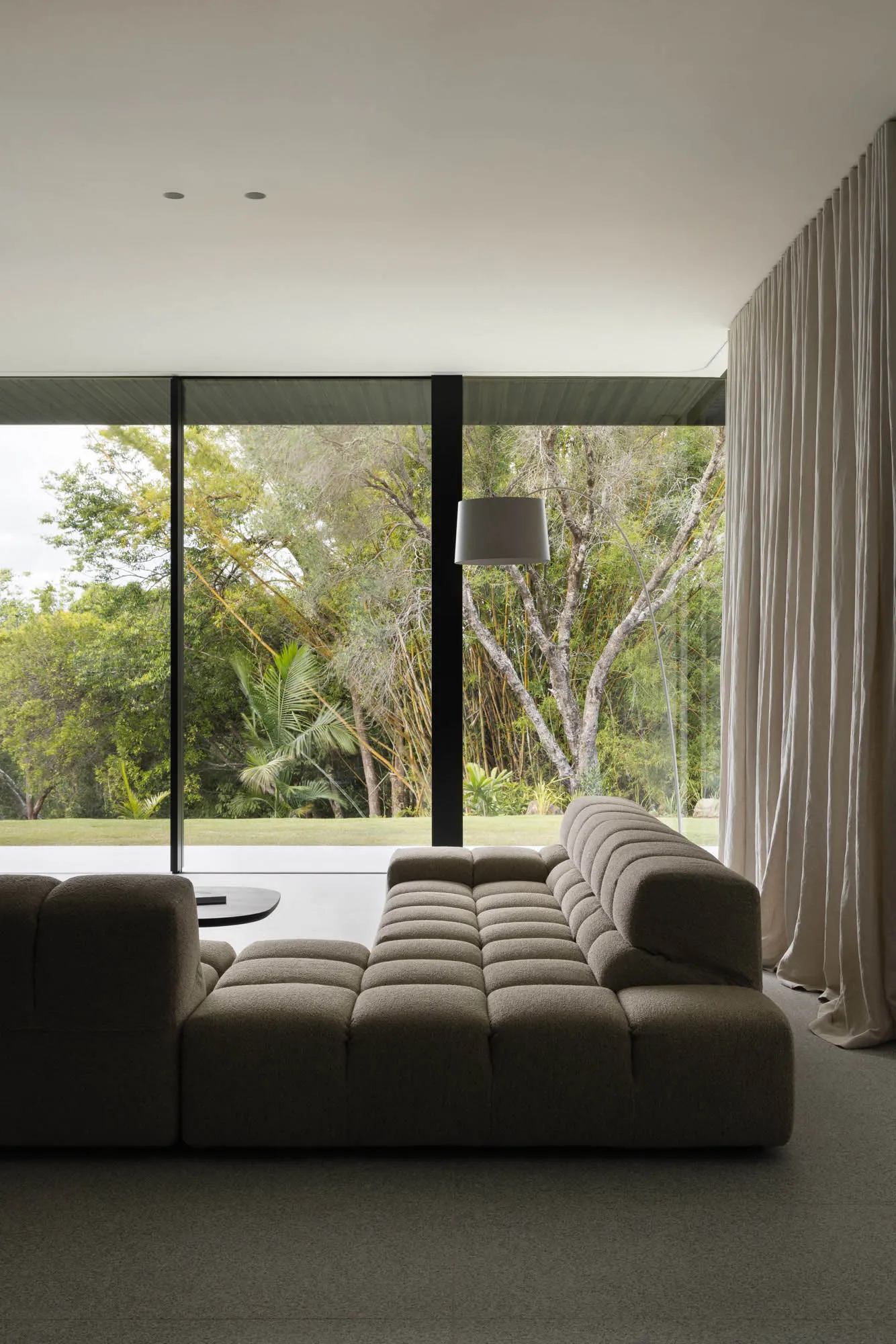 Modern living room with a textured couch and glass windows overlooking greenery.