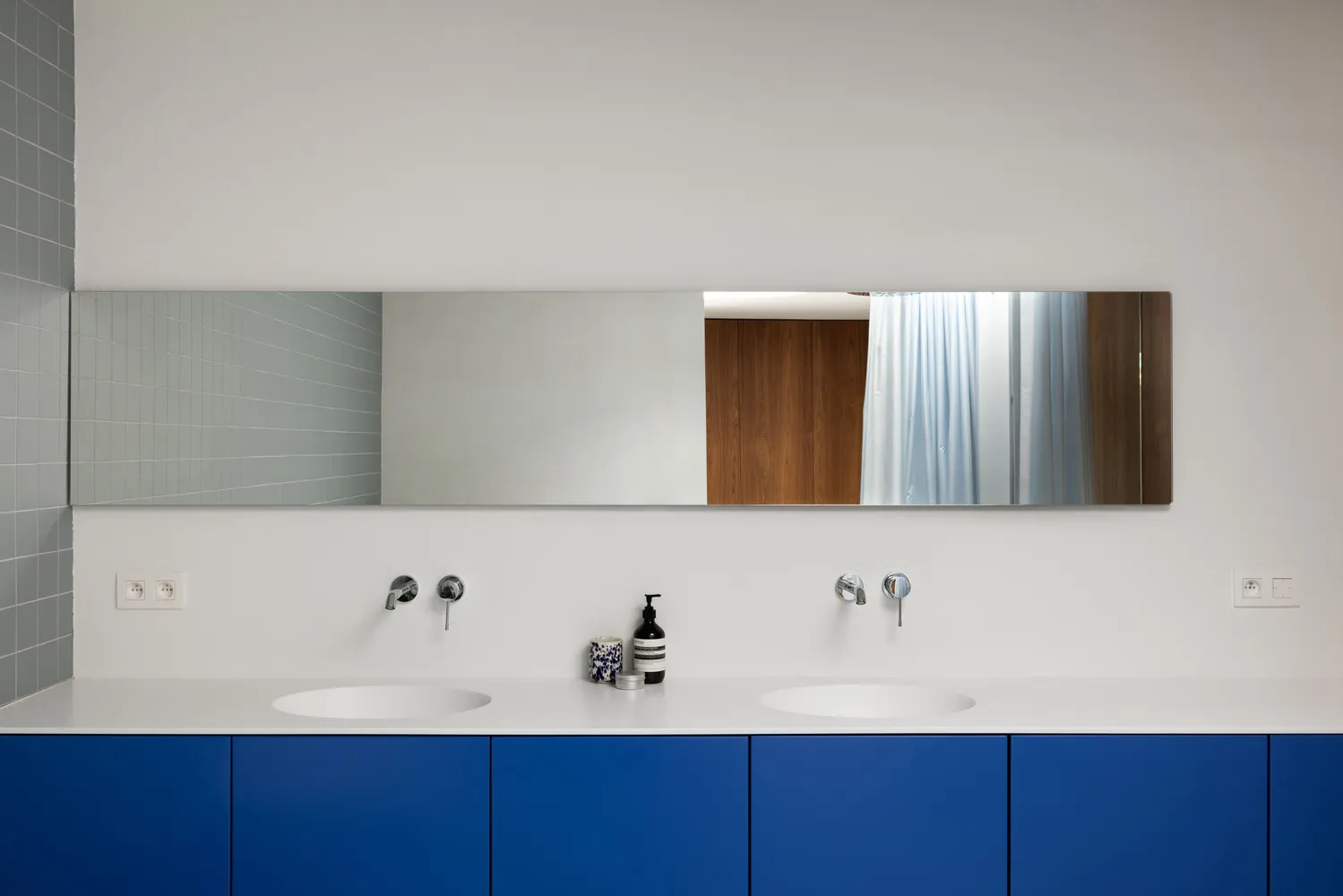 Minimalist bathroom with blue cabinets, metallic faucets, and wood accents.