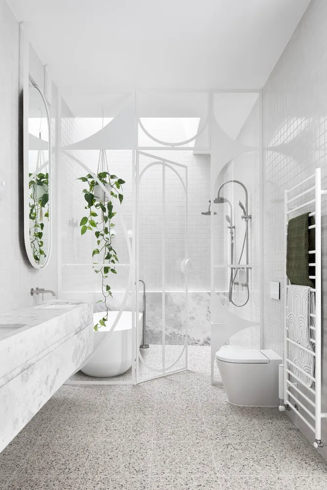A modern bathroom featuring white terrazzo flooring and minimalist white fixtures, with a single potted plant and a large mir