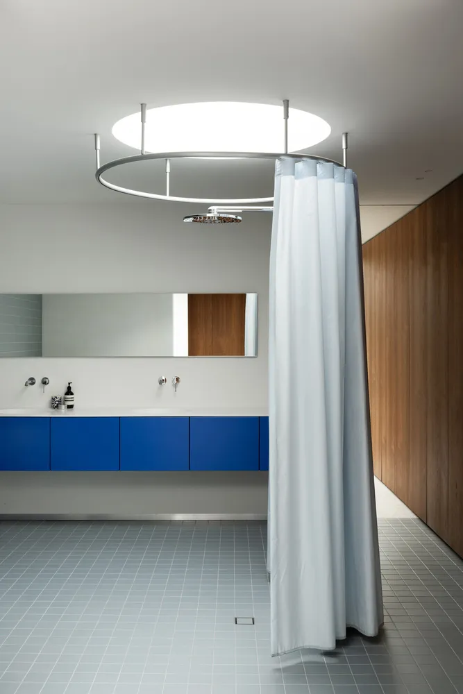 A modern bathroom featuring white glass shower enclosure, blue storage cabinets, and wooden accents.