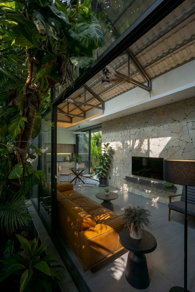 A modern living room featuring glass walls, stone accents, and concrete floors, with a comfortable seating area and a flat-sc