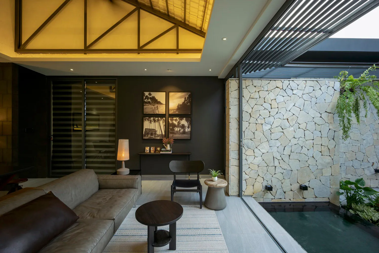 A contemporary living room featuring concrete and stone materials, with a dark sofa, wooden table, and artistic wall decor.